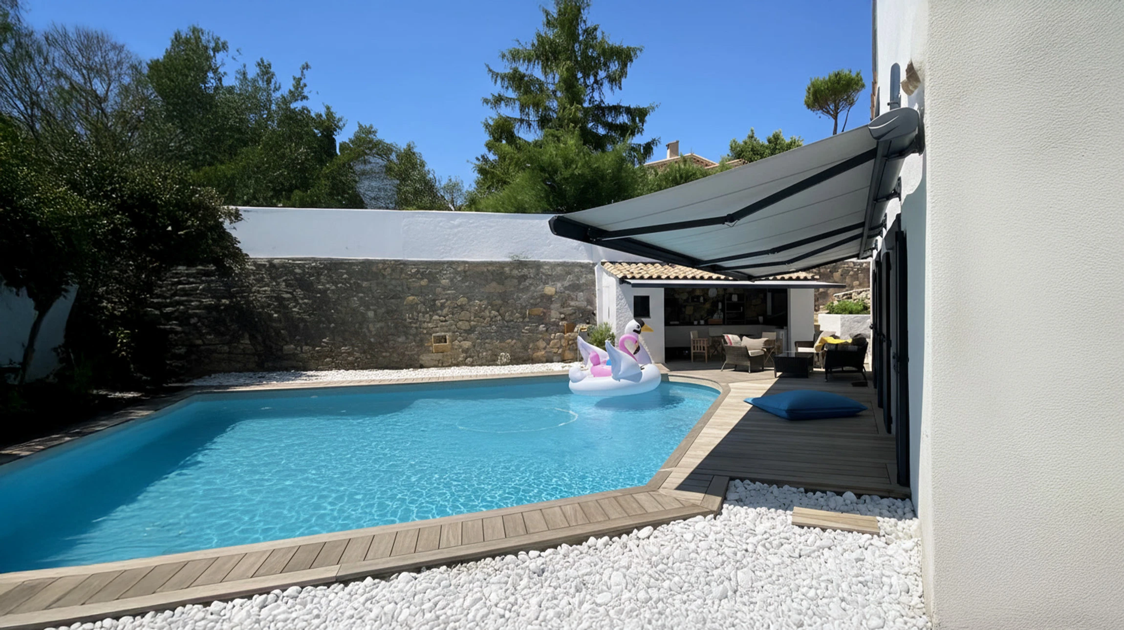 Terrasse extérieure avec piscine rectangulaire à eau turquoise, personne sur bouée licorne gonflable rose et blanche