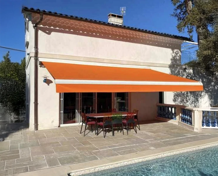 Terrasse extérieure d'une villa avec piscine, équipée d'une table et chaises sous store banne orange déployé